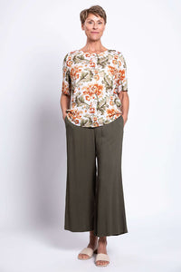 Full body view of woman wearing floral blouse and olive pants, hands in pockets
