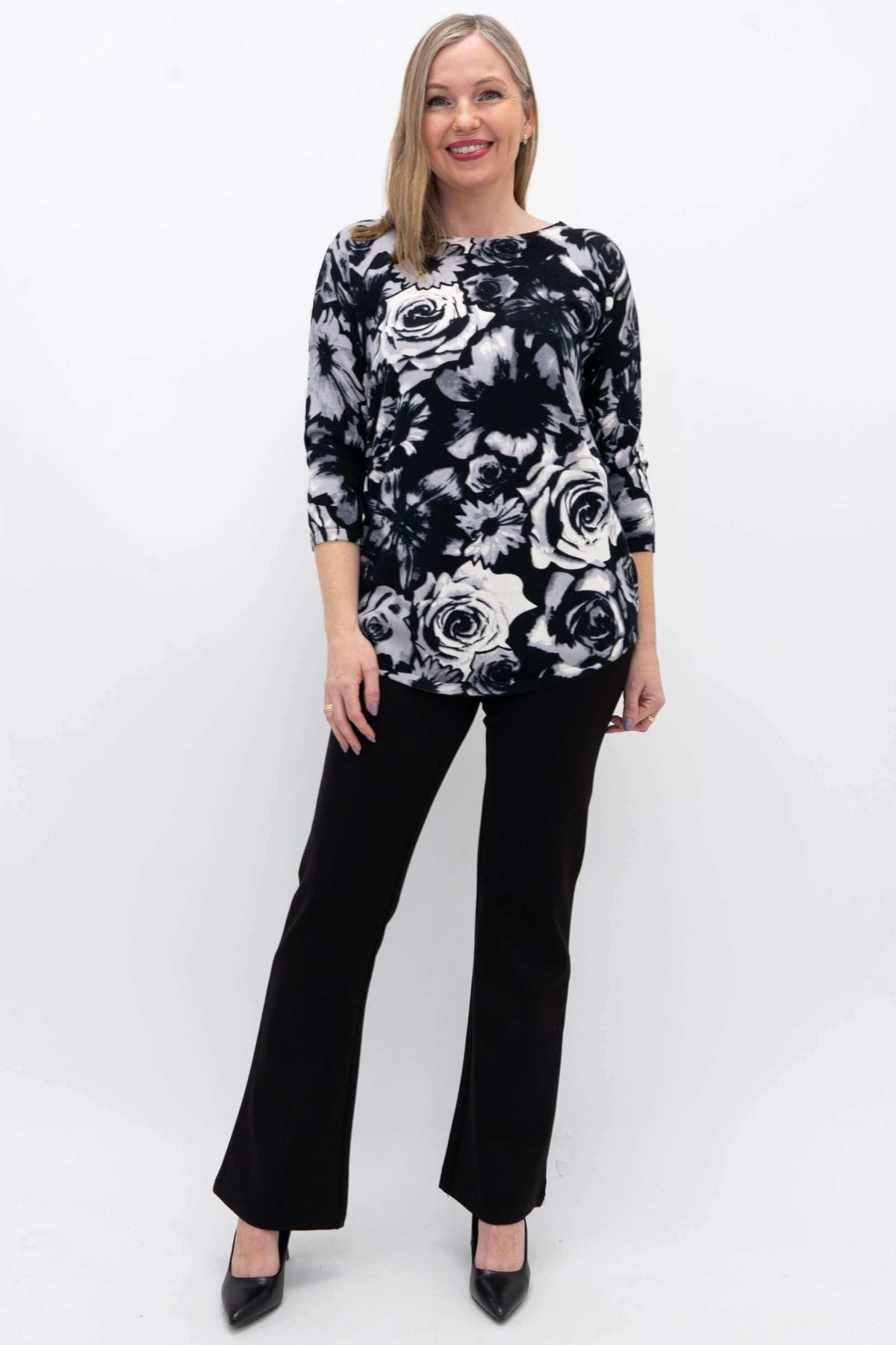 Full body view of a woman modeling a black and white floral pullover sweater with black pants