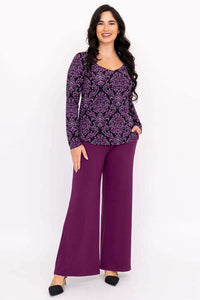 Woman smiling in full outfit with purple damask print top and purple pants