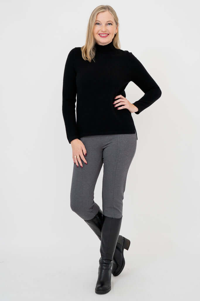 Full body view of woman in black mock neck sweater, grey pants, and black boots