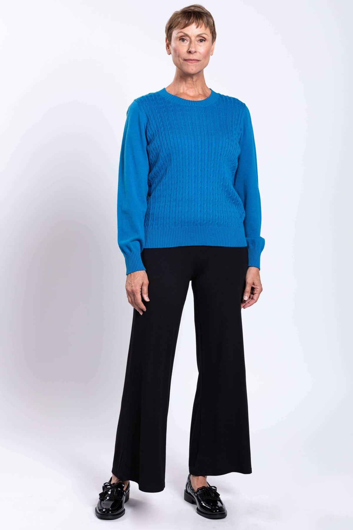 Full body view of woman wearing a blue cable knit sweater and black pants
