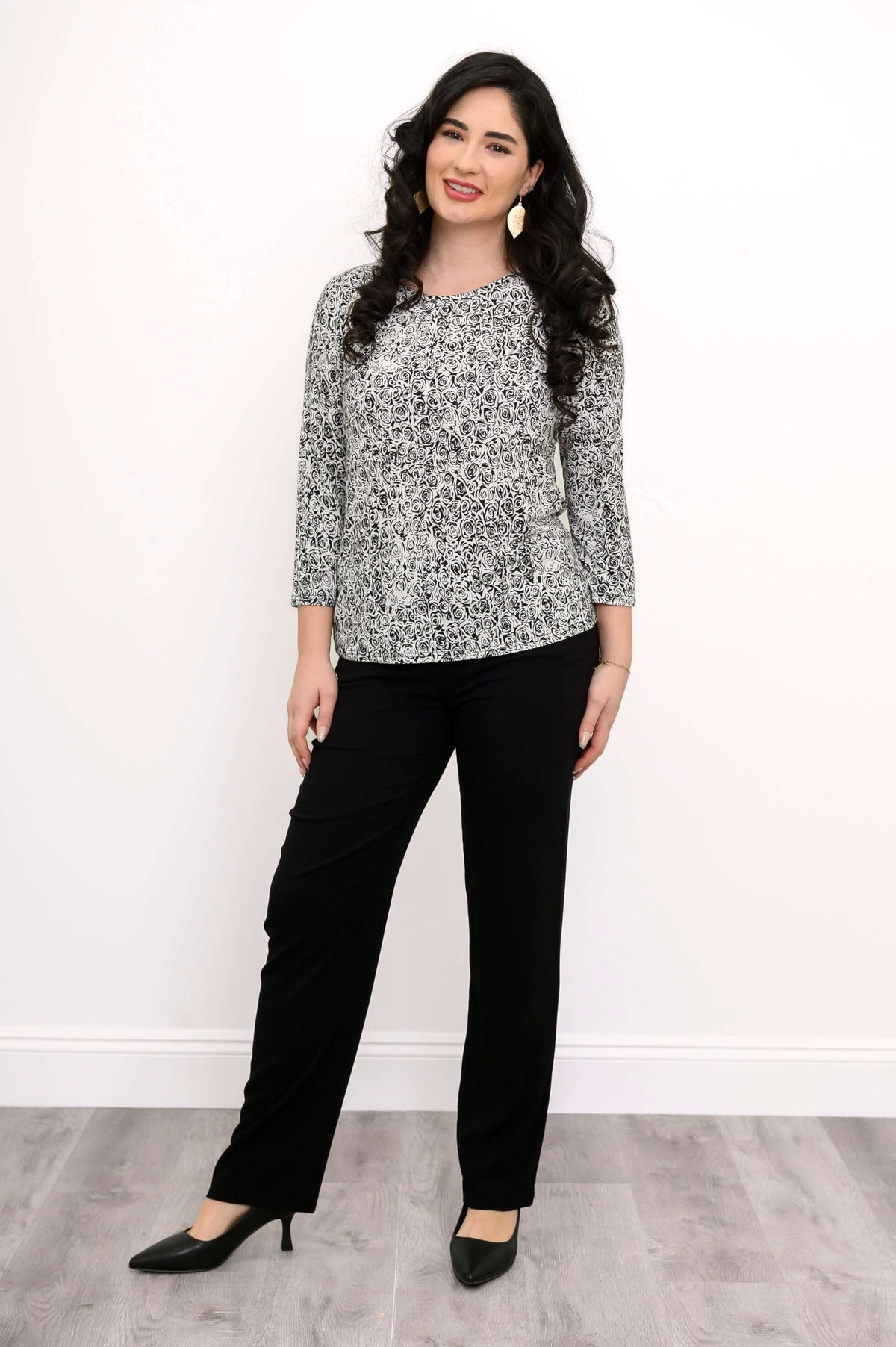 Full body view of a woman in a black-and-white rose print fitted top and black pants