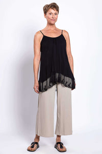 Full body view of a woman in a black lace-trimmed tank top and light-colored pants