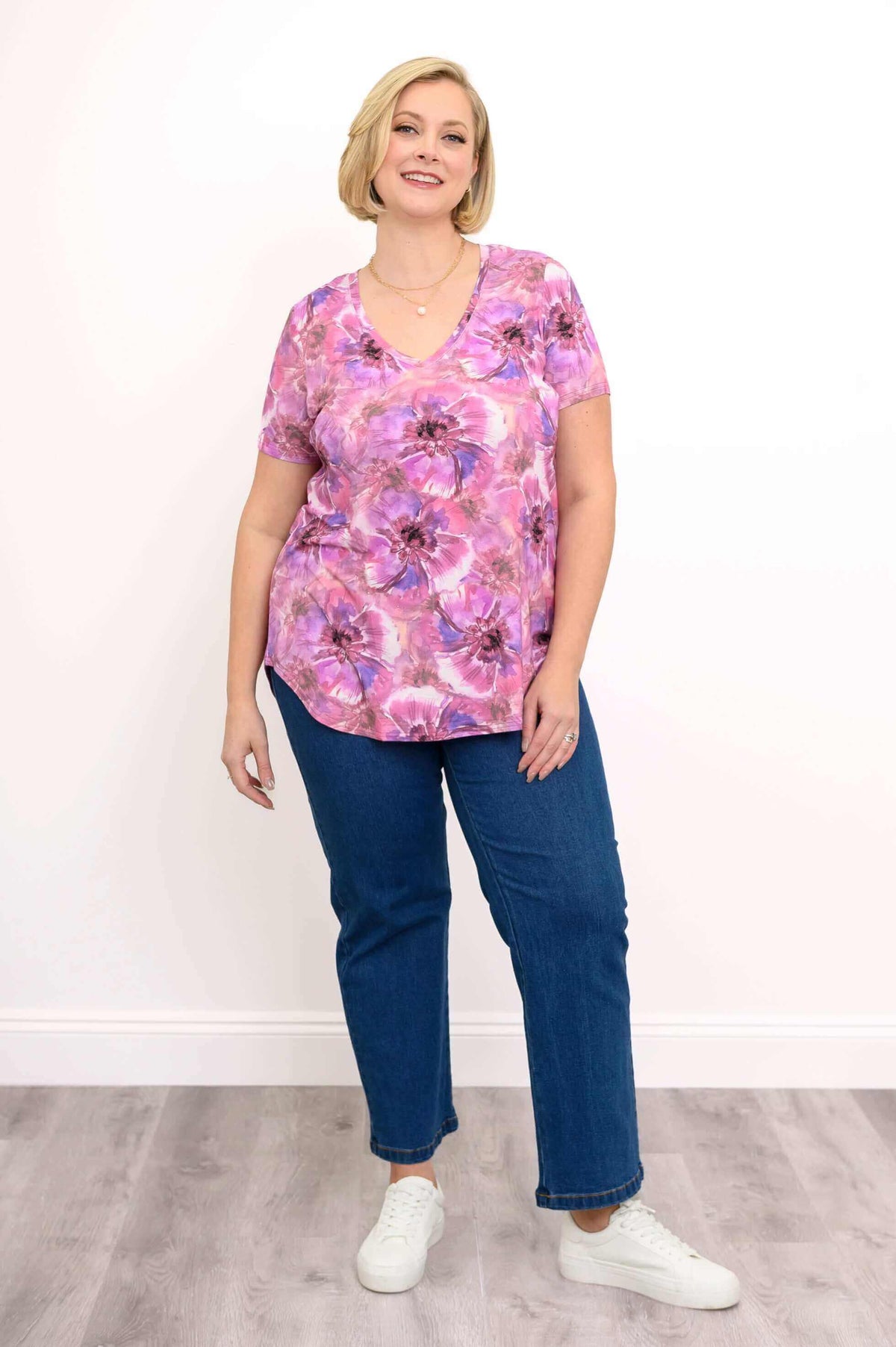Full body view of woman in pink floral bamboo top with blue jeans and white sneakers
