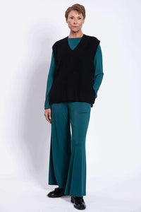 Full body view of model in black oversized sweater vest with teal top and wide-leg pants