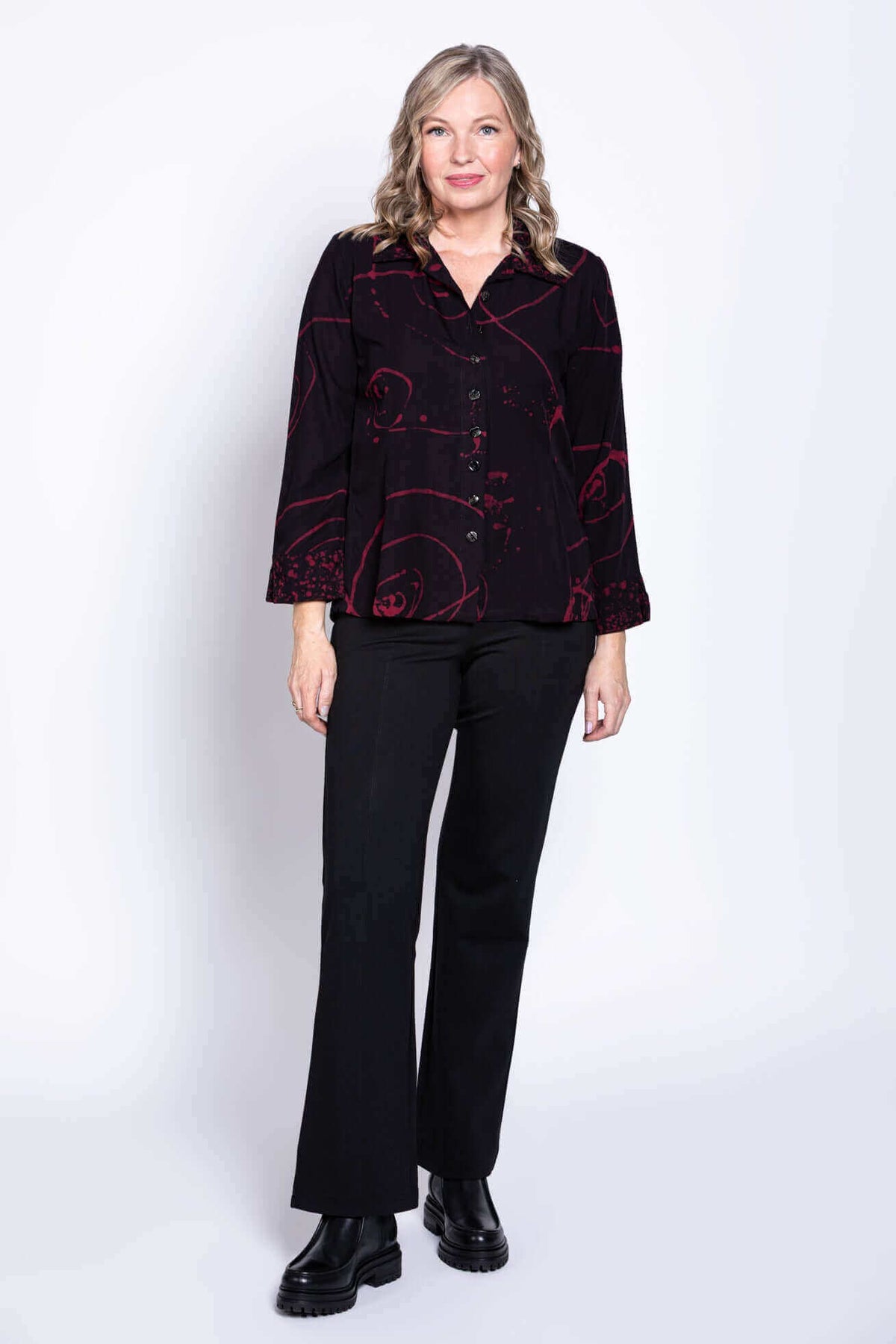 Full body view of a woman modeling a black shirt with red swirl print and black pants