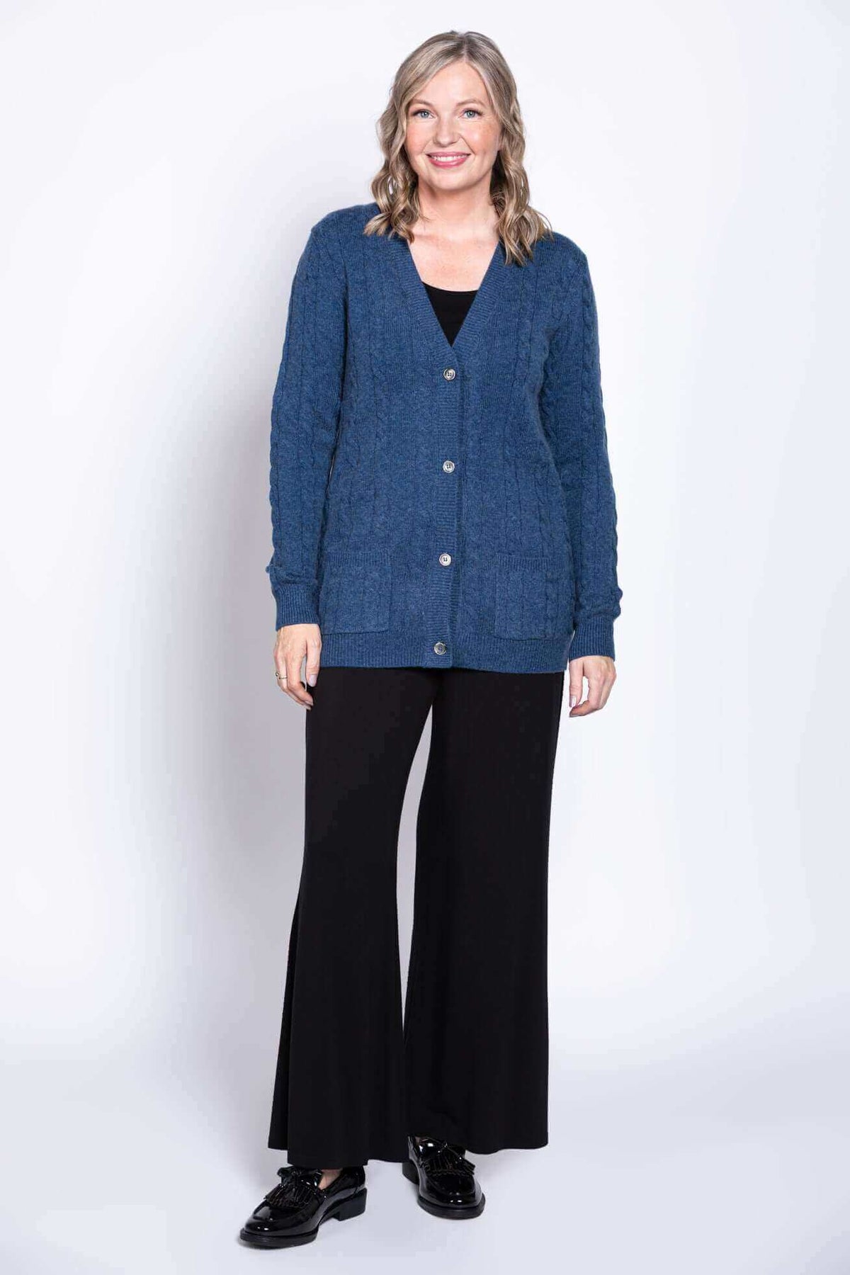 Full body view of woman in blue cable knit cardigan and black pants