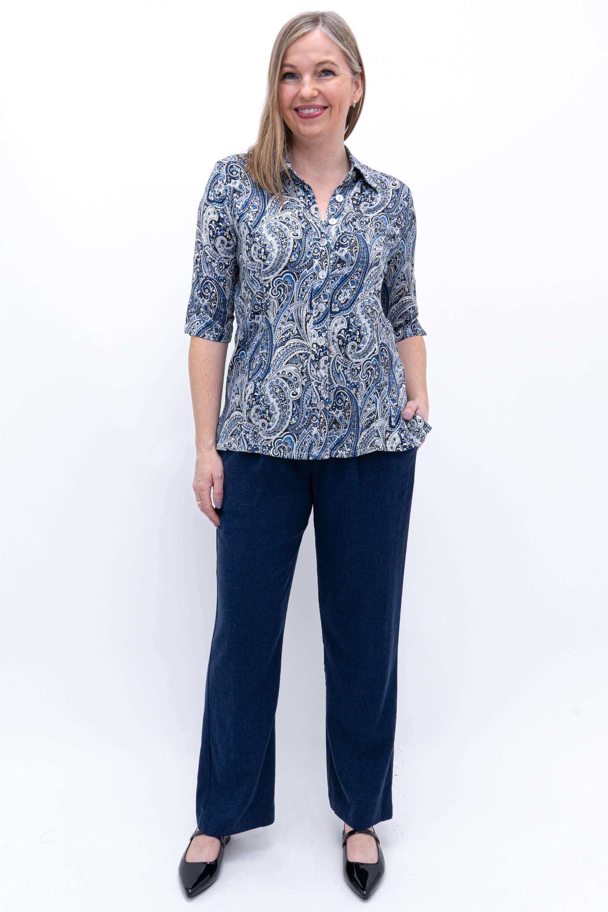Full body view of woman in blue paisley blouse and navy pants, standing against white background