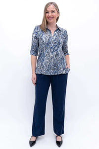 Full body view of woman in blue paisley blouse and navy pants, standing against white background