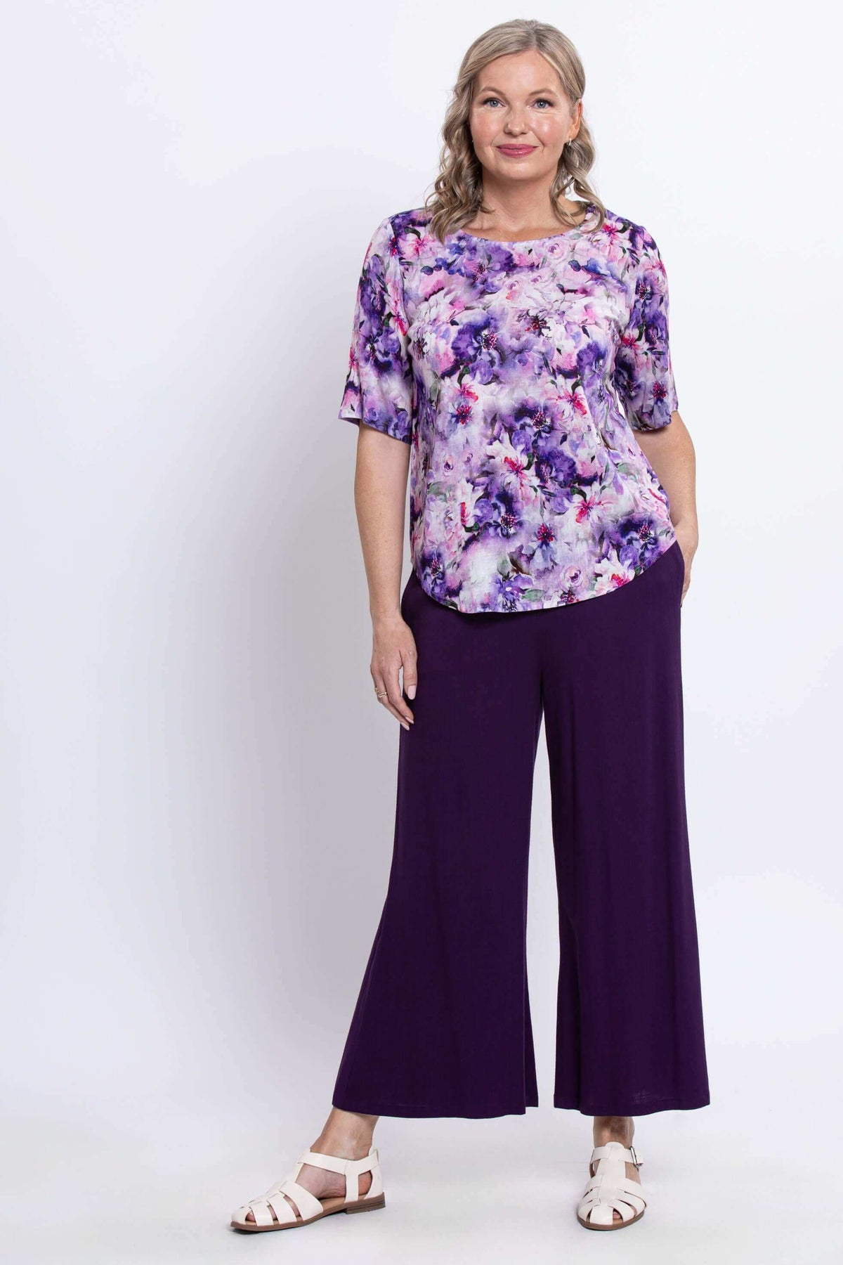 Full body view of woman in floral blouse and wide-leg purple pants, facing forward
