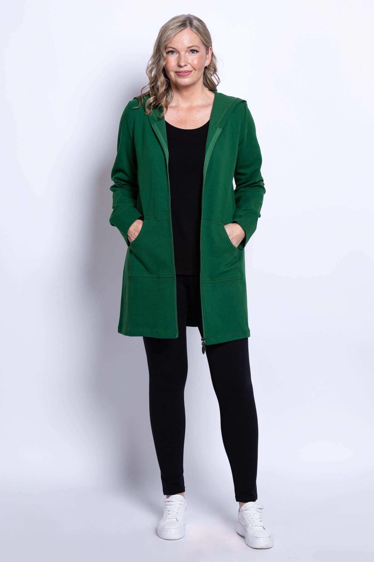 Full body view of a woman in a green hooded jacket with zip front and black leggings