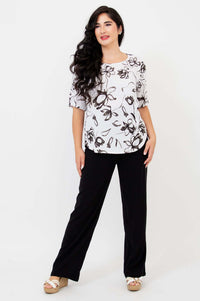 Woman posing in white floral print blouse and black pants, full body view