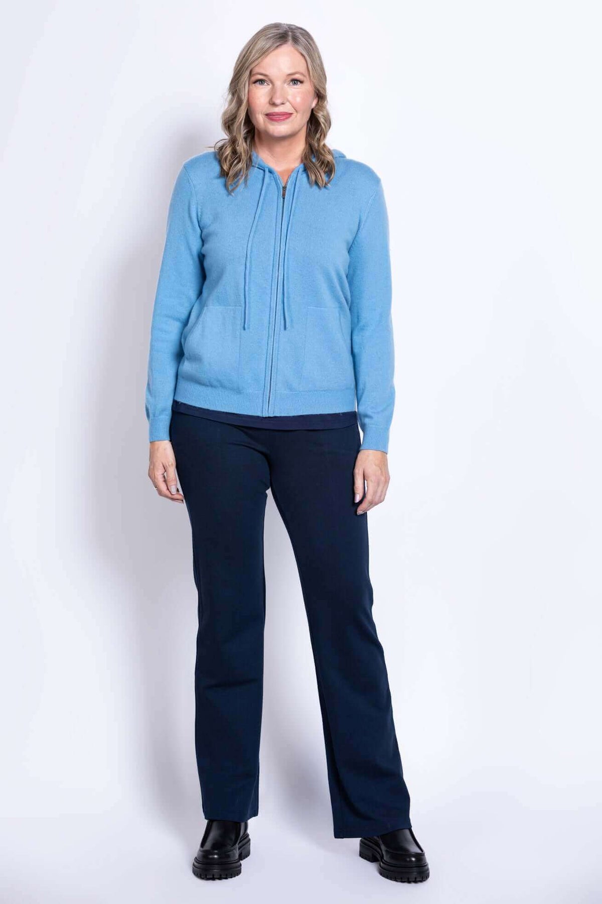 Straight-on full body view of woman in blue zip hoodie and navy pants