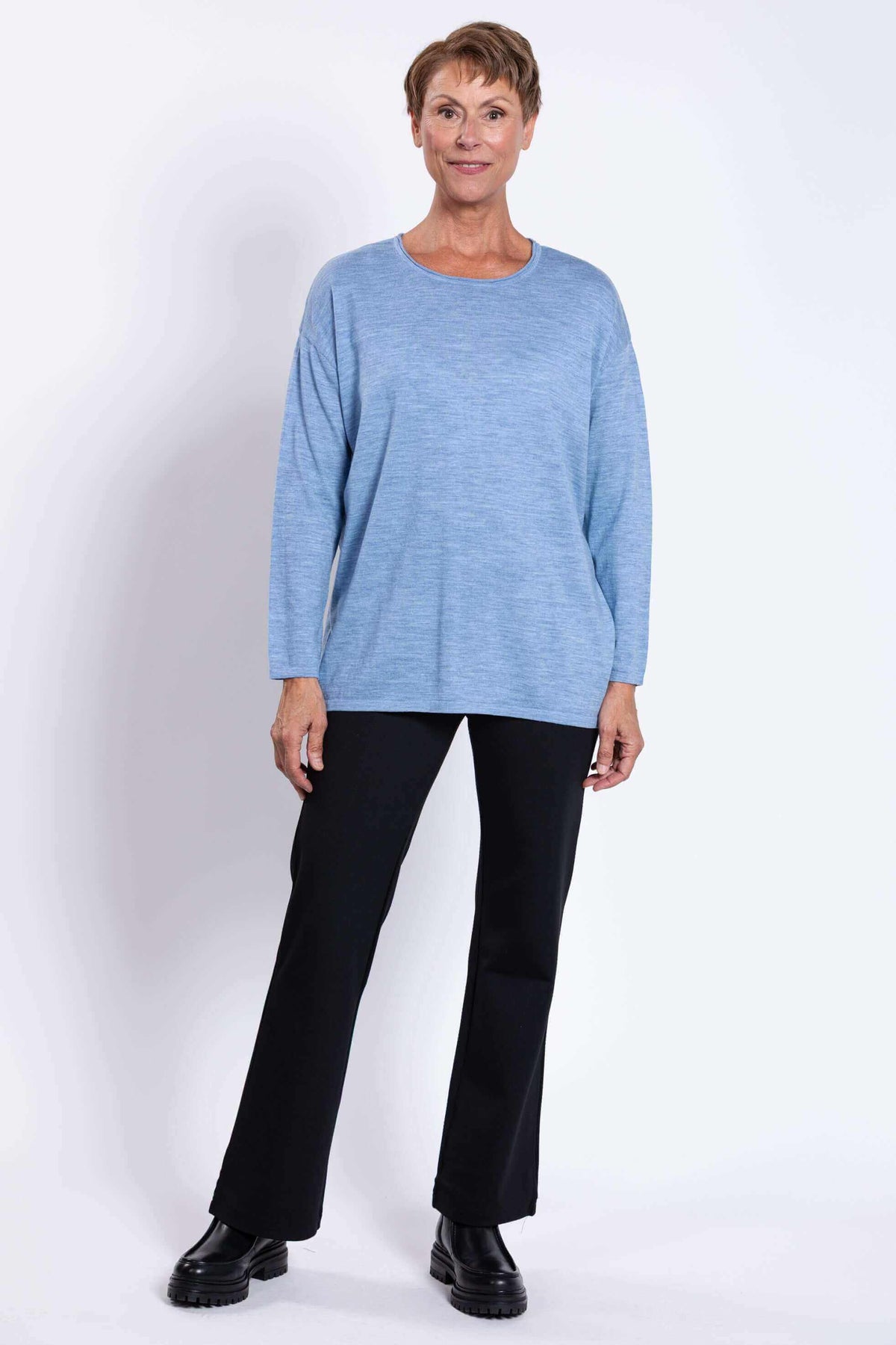 Full body straight front view of woman in light blue sweater and black pants