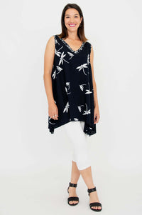 Full body view of woman in black sleeveless tunic with white floral pattern and white leggings