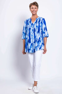 Full body shot of a woman in a blue tie-dye Margate blouse and white cropped pants