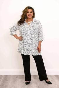 Full body view, hands on hips, wearing white petal print tunic top and black straight pants