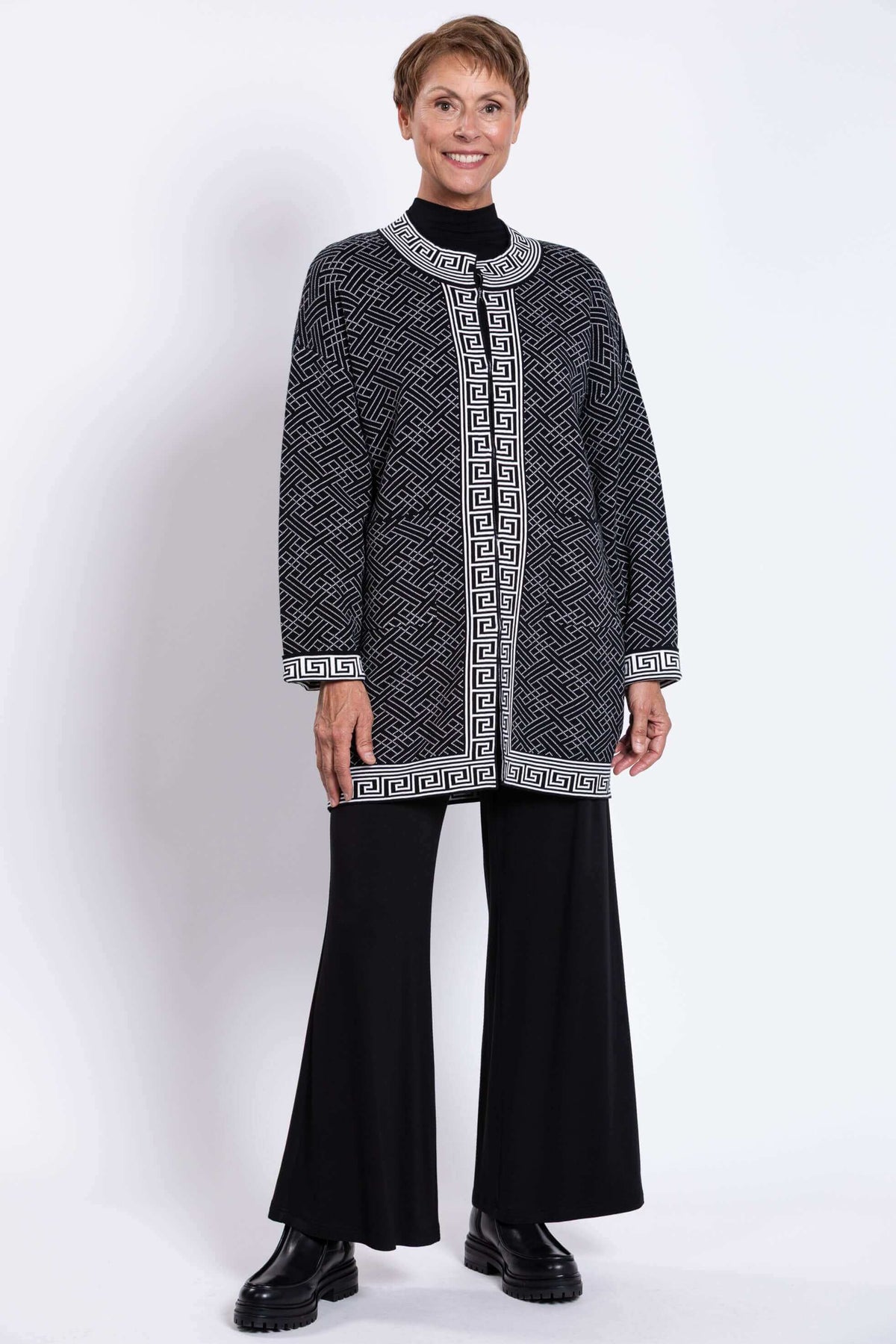 Full body view of a model in a black and white geometric print cardigan and black pants