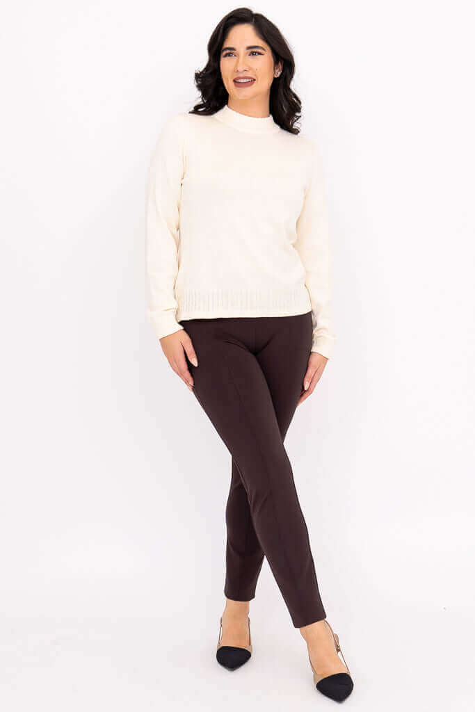 Full body shot of a model showcasing an ivory mock neck knit pullover top styled with dark pants.