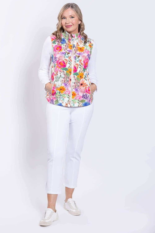 Full body view of woman wearing a pink floral vest and white pants with hands in pockets