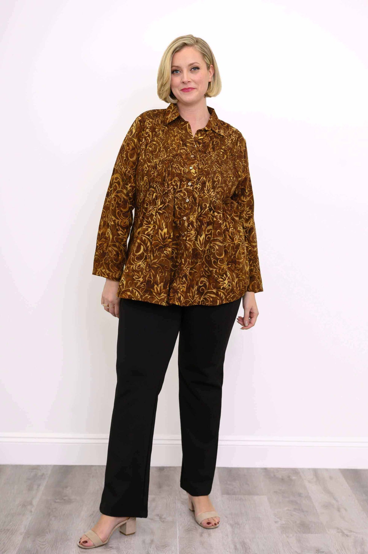 Full body view of woman modeling an autumn gold smocked button-up shirt with black pants