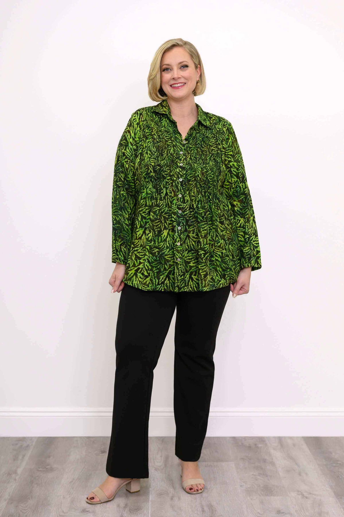 Woman wearing green leaf print smocked top with black pants, full body view