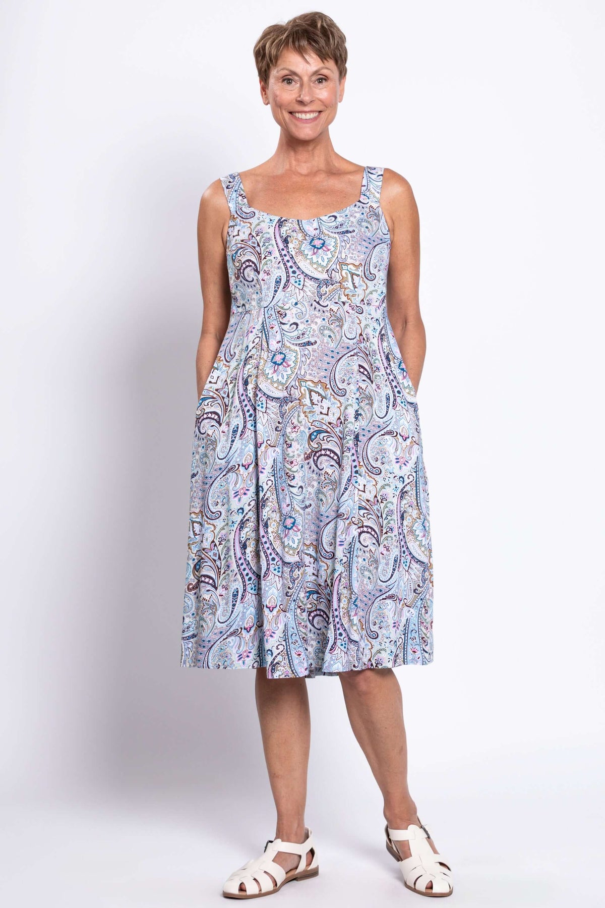 Woman in sleeveless paisley print dress with scoop neckline and pockets, full length