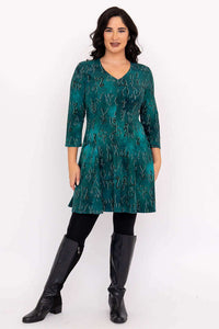 Full length view of a woman in a teal abstract print tunic dress, black leggings, and leather boots.