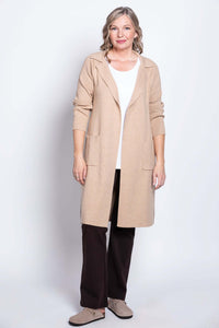 Full body view of a woman in a beige open front cotton jacket, white shirt, and brown pants