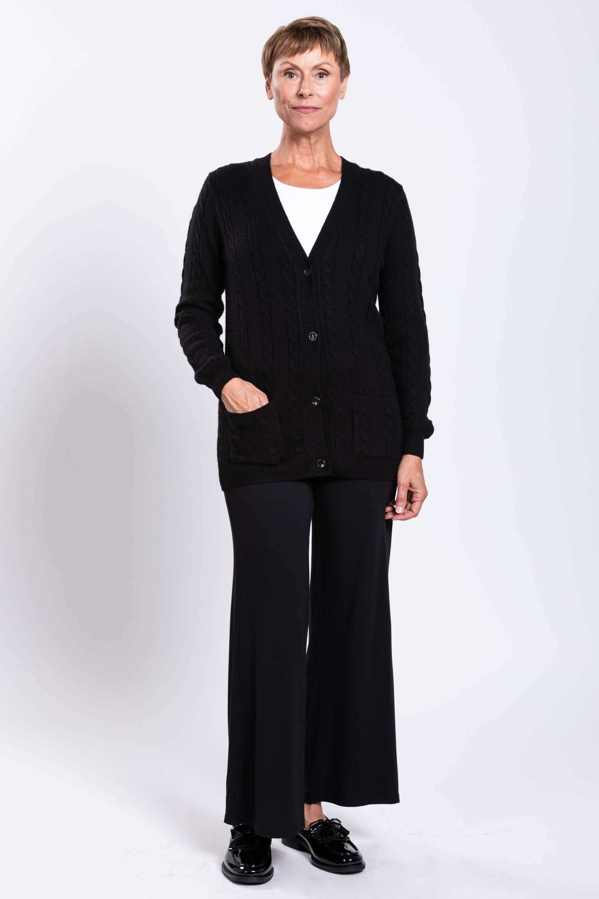 Full body view of a woman in a black cable knit cardigan and wide-leg pants