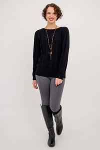 Full length view of a woman in a black cable knit sweater, grey pants, and black boots