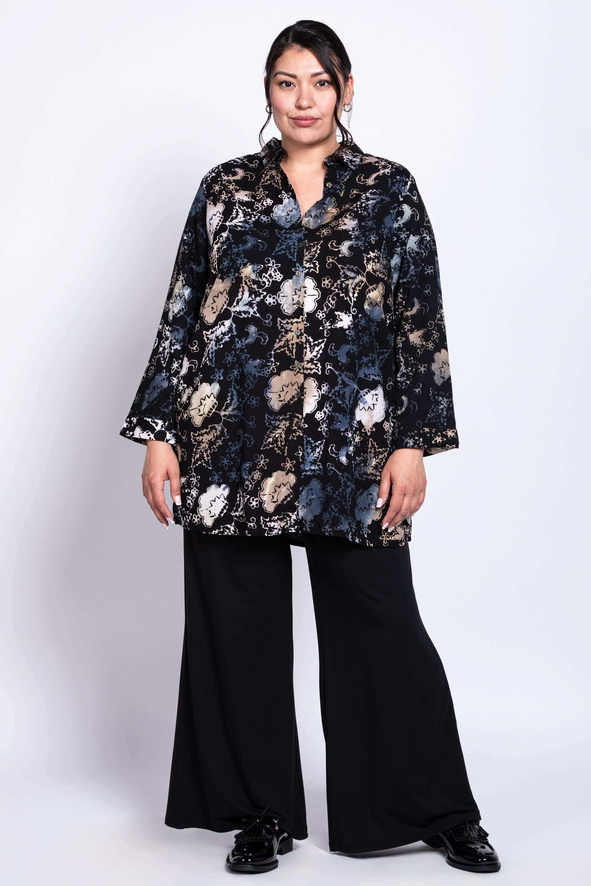 Full body view of model in black floral batik print tunic shirt and wide-leg pants
