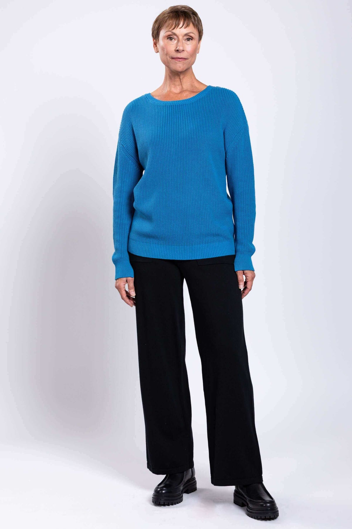 Full body view of model in blue shaker stitch sweater and black pants