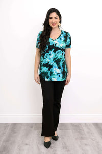Full body view of model smiling in bright turquoise printed top black pants, and black shoes