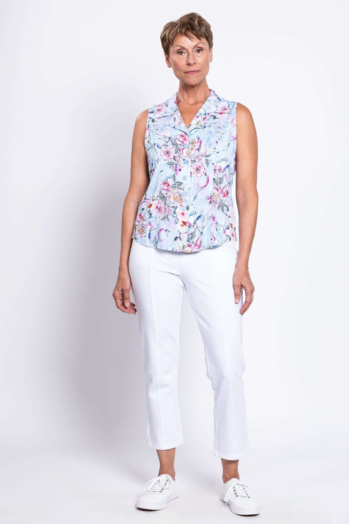 Full body view of woman in a sleeveless floral print shirt paired with white cropped pants