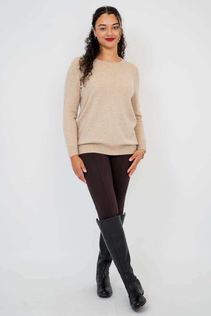 Full body view of woman in beige sweater, brown pants, and black boots
