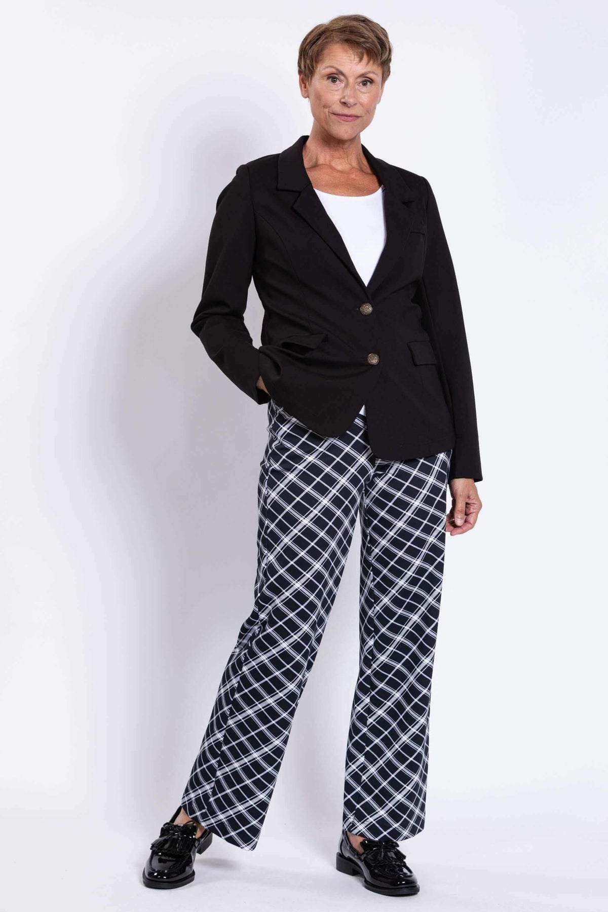 Full body view of woman in black blazer and checked pants with one hand in pocket