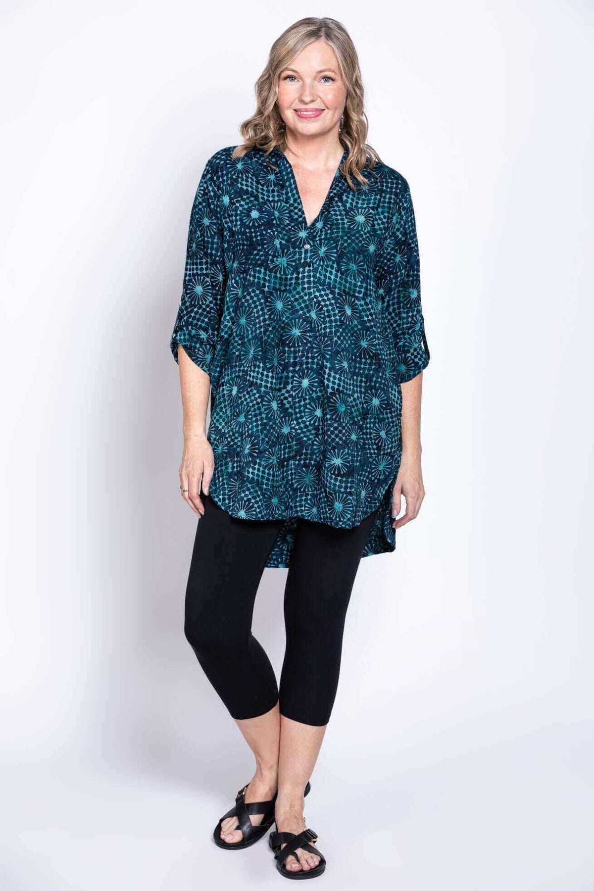 Full body view of woman in blue batik blouse, black leggings, and sandals