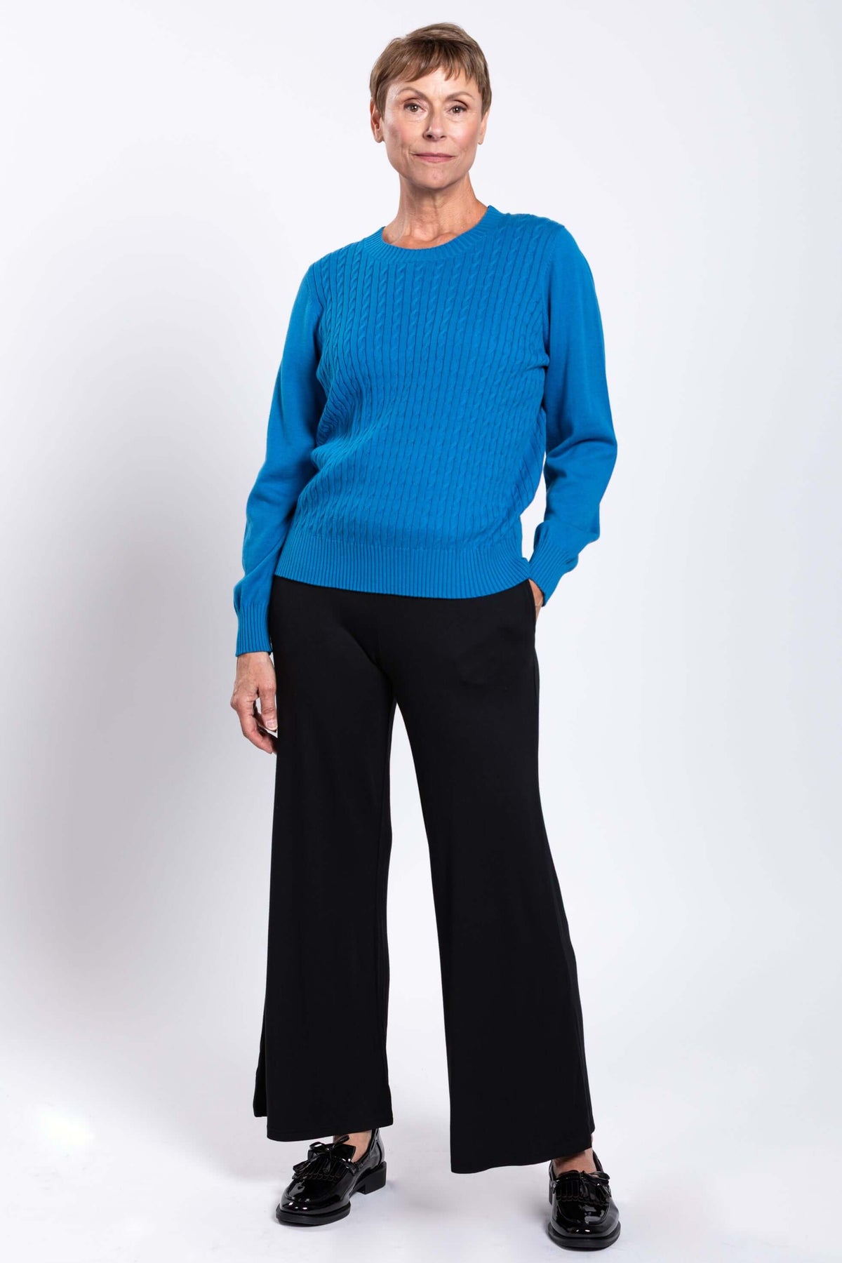 Full body view of woman in blue cable knit sweater and black pants