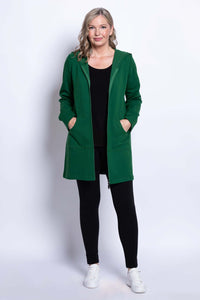 Woman standing, wearing a green hooded jacket with black leggings and white sneakers