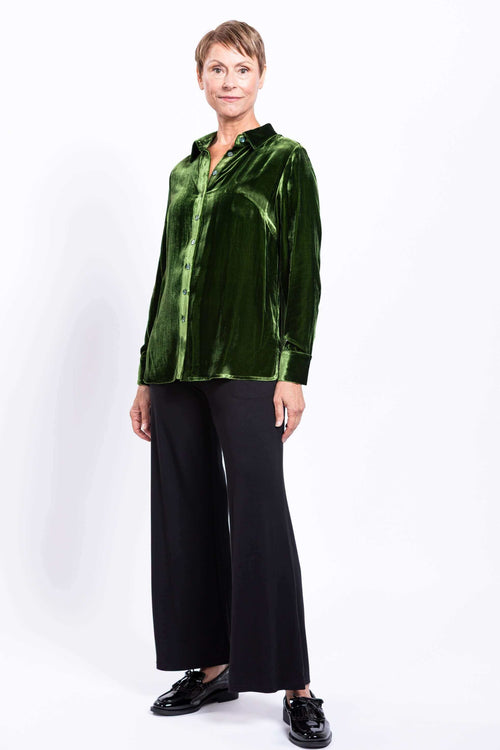 Woman standing in green silk velvet blouse and black wide-leg pants, full body front view