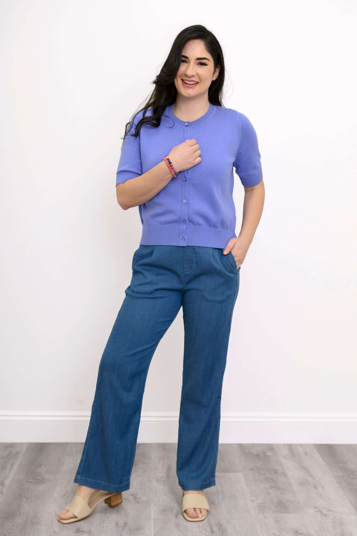 Woman wearing a lavender cardigan, one hand on chest, full body view