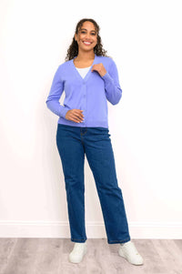 Full body view of woman in light purple V-neck button-up cardigan, blue jeans, and white sneakers