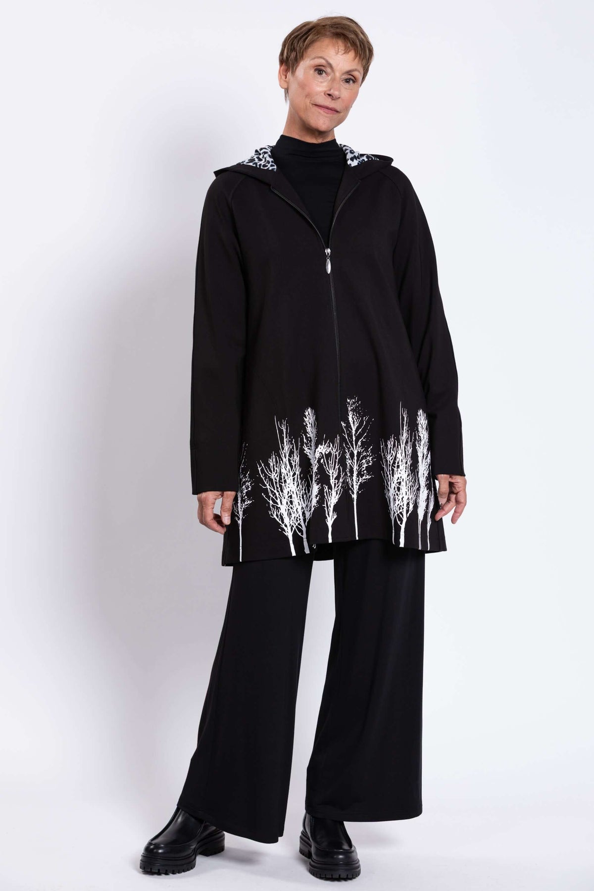 Full body view of woman modeling black Edith Coat with white tree border