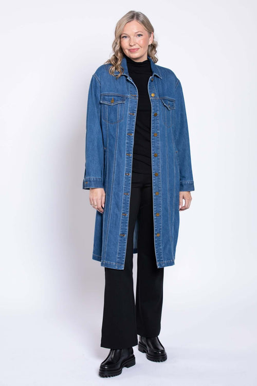 Full body view of woman modeling longline blue denim jacket with black pants and boots