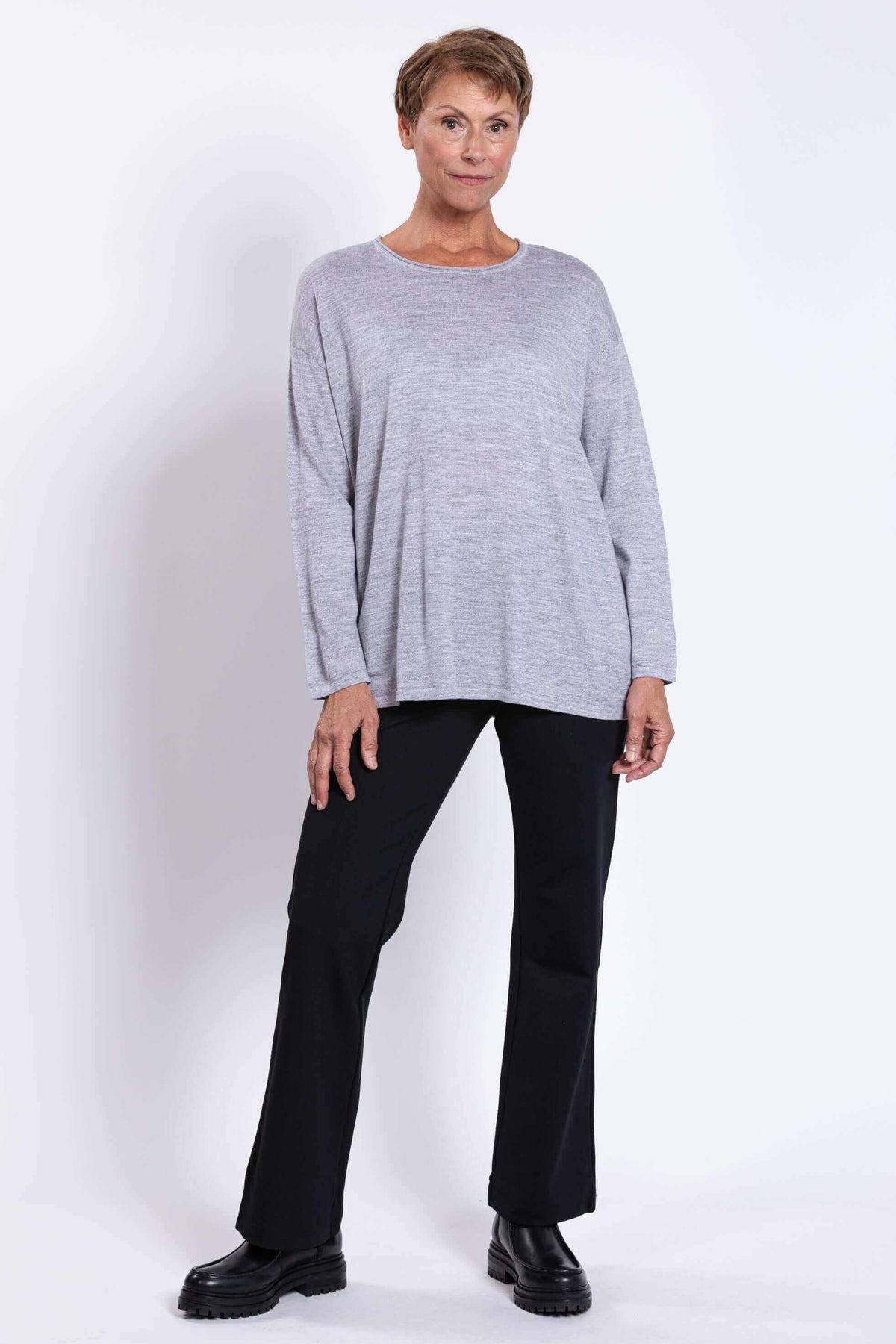 Full body view of woman in a light grey merino sweater and black pants