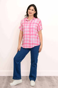 Full body shot of a woman in a pink plaid blouse and blue jeans, standing indoors