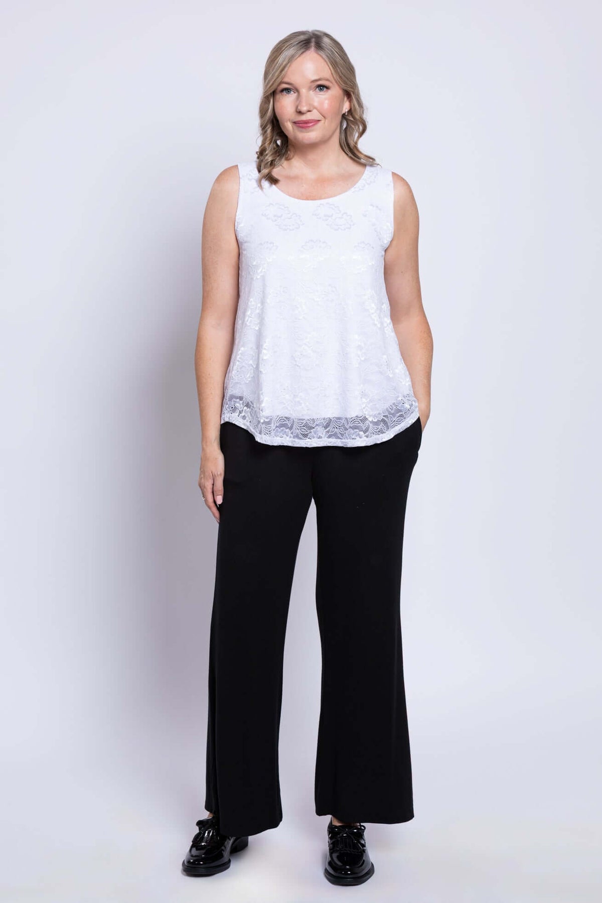 Full body view of woman wearing white lace tank top and black pants