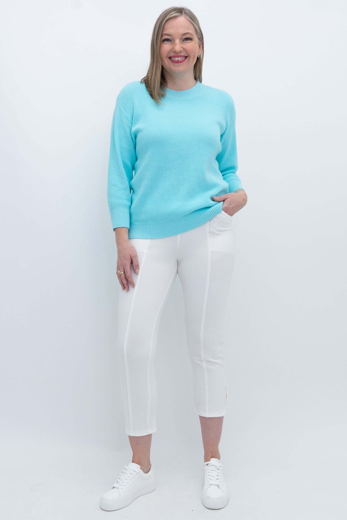 Full body view of woman in light blue sweater with white pants and sneakers