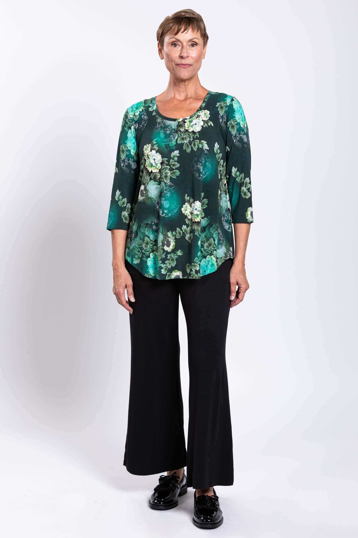 Full body front view of woman in green floral bamboo top and black wide leg pants